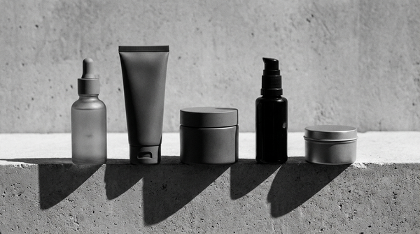Linea skincare completa da uomo: cinque prodotti viso disposti in griglia su superficie di cemento