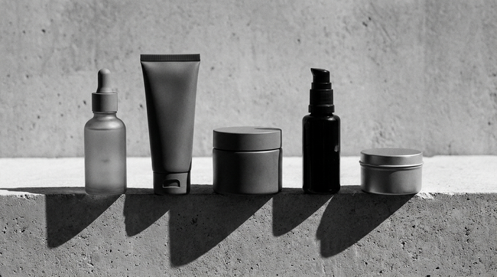 Linea skincare completa da uomo: cinque prodotti viso disposti in griglia su superficie di cemento