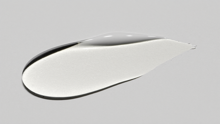 Goccia di siero alla niacinamide su superficie chiara, macro editoriale monocromo HBSKN