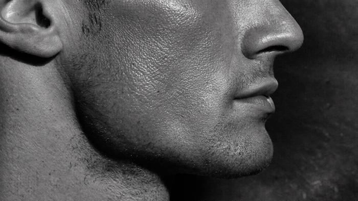 Pelle grassa viso uomo: macro della cute maschile con pori visibili e lucido da sebo in luce drammatica, estetica lab HBSKN